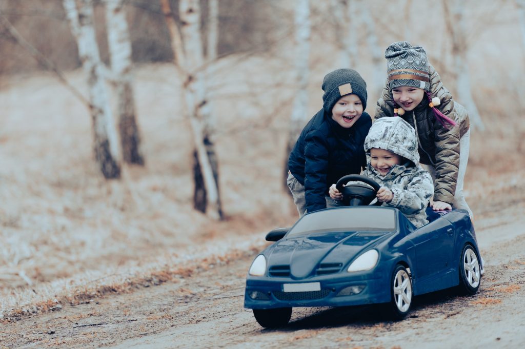 Three happy kids driving a blue toy car, road trips adventure concept
